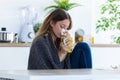 Illness young woman sneezing in a tissue while drinking hot beverage in the kitchen at home