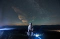 Illuminated man wearing white space suit and helmet sitting on a bench on a hill at night
