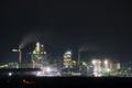 Illuminated cement plant with high factory structure and tower cranes at industrial production area at night