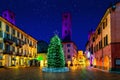 Illuminated Christmas tree on town square among old historic buildings in Alba, Italy