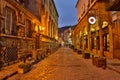 Illuminated cobbled street with light reflections on cobblestones in old historical city by night. Dark blurred