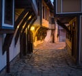 Illuminated cobbled street with light reflections on cobblestones in old historical city by night. Dark blurred