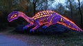 Illuminated dinosaur sculpture resting on a rock in a park at twilight. Vibrant colors and patterns create a striking visual Royalty Free Stock Photo
