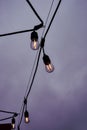 Illuminated Edison lightbulbs in row on black wire against gray cloudy sky Royalty Free Stock Photo