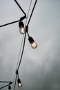 Illuminated Edison lightbulbs in row on black wire against gray cloudy sky