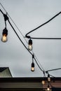 Illuminated Edison lightbulbs in row on black wire against gray cloudy sky