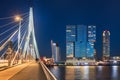 Illuminated Erasmus bridge and Rotterdam building at nighttime.