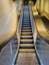 Illuminated escalator next to a staircase of the Paris metro. White tiled wall