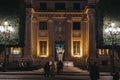 Illuminated facade of Banco de Espana in Seville, Spain, at night, people in front