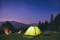 Illuminated green tent under stars at night forest