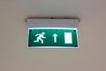 Illuminated green and white exit sign on the ceiling in a public place. Royalty Free Stock Photo