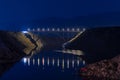 Illuminated highway bridge under stars, reflection of lights in water, mountains in background and bright stars in sky Royalty Free Stock Photo