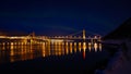 Illuminated Kvalsund bridge near Hammerfest, Norway at night in winter with slightly visible aurora and reflections in water.