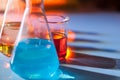 Illuminated laboratory flask filed with colorful chemical solutions with shadows on the table. Laboratory, science