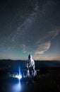 Illuminated man wearing white space suit and helmet sitting on a bench on a hill at night