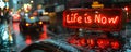 Illuminated neon sign in a rainy cityscape boldly declaring Life is Now, emphasizing the concept of living in the moment and Royalty Free Stock Photo