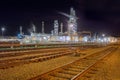 Illuminated oil refinery at night with rail tracks on the foreground