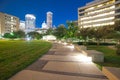 Illuminated pathway concrete sidewalk at park square with downtown Houston skyscraper, capitol tower in background during evening