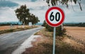 Illuminated photo of European speed limit road sign - 60 with road and field on background. Red traffic sign symbol with maximum