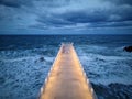 illuminated pier with dramatic sky over stormy dark sea at evening Royalty Free Stock Photo