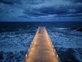 illuminated pier with dramatic sky over stormy dark sea at evening Royalty Free Stock Photo