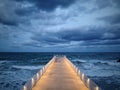 illuminated pier with dramatic sky over stormy dark sea at evening Royalty Free Stock Photo