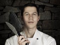 Illuminated portrait of nice and attractive man chef in uniform on the stone wall background. Man chef posing to camera with knif Royalty Free Stock Photo