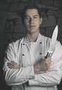 Illuminated portrait of nice and attractive man chef in uniform on the stone wall background. Man chef posing to camera with knif Royalty Free Stock Photo