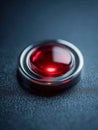 Illuminated red round button with metallic silver rim on textured dark surface symbolizing alert or activation in modern Royalty Free Stock Photo