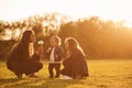 Illuminated by sunlight. Playing with dandelion. Woman with her two young daughters is on the summer field