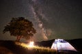 Illuminated tent near campfire and big tree at night in mountains under starry sky with Milky way Royalty Free Stock Photo