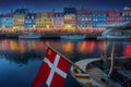 Illuminated view of Nyhavn port and waterfront at night with the flag of Denmark - Copenhagen, Denmark