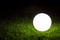 Illuminating a spherical ground garden lamp of white color lies on a green lawn. Royalty Free Stock Photo