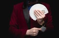 Illusionist man shows fan of playing cards takes ace out hand on black background Royalty Free Stock Photo