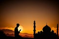 Illustration of Silhouette of a devout Islamic man pray to the Allah on hill, outside mosque, at sunset