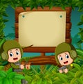 Two soldiers with guns in the jungle with wooden signboard