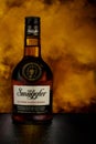 Illustrative editorial bottle of Scotch whiskey Old Smuggler on a background of golden smoke.