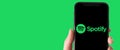 Illustrative photo of a hand holding a smartphone with the Spotify logo on screen - Horizontal banner web