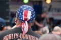 Harley Dadidson biker with american flag on head on back view at rock n roll concert at fun car show event