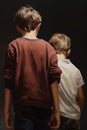 A boy harassing a younger boy with a black background representing bullying, back view, vertical