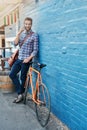 Im hopping on my bike now. a handsome young man leaning against a wall with his bike talking on a cellphone. Royalty Free Stock Photo