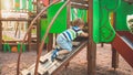 Photo of adorable toddler boy climbing and crawling on wooden staircase on children palyground at park