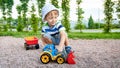 Photo of adorable 3 years old toddler boy playing with sand and you truck and trailer in park. Child digging and Royalty Free Stock Photo