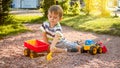 Photo of adorable 3 years old toddler boy playing with sand and you truck and trailer in park. Child digging and Royalty Free Stock Photo