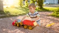 Photo of adorable 3 years old toddler boy playing with sand and you truck and trailer in park. Child digging and Royalty Free Stock Photo