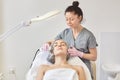 Image of adorable young woman getting ultrasonic facial cleanse, professional cosmetologist making ultrasound face cleaning Royalty Free Stock Photo