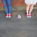 An image of adults in red sneakers next to baby pair of sneakers