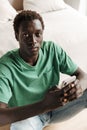 Image of african american man holding smartphone while sitting at home