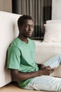 Image of african american man holding smartphone while sitting at home