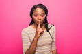 Portrait of african woman holding index finger on lips and asking to keep silence isolated over pink background Royalty Free Stock Photo